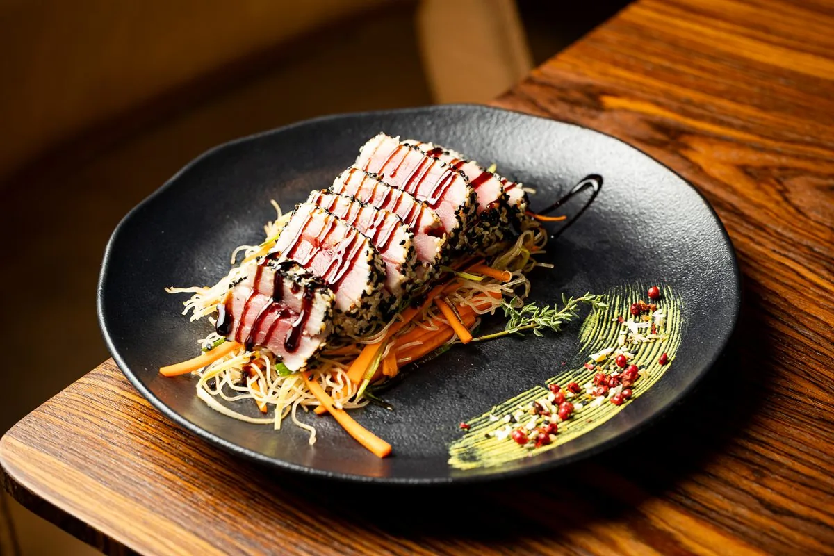 Prato elegante com peixe em crosta, legumes finos e molho escuro