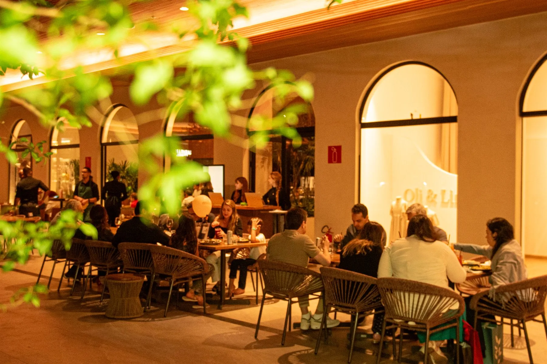 Pessoas à mesa entre salão e varanda à noite